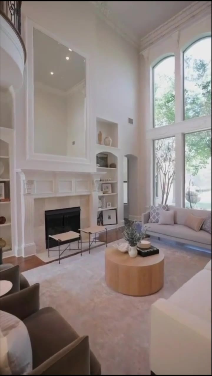 A double-height great room in white, with a mirror over the fireplace.