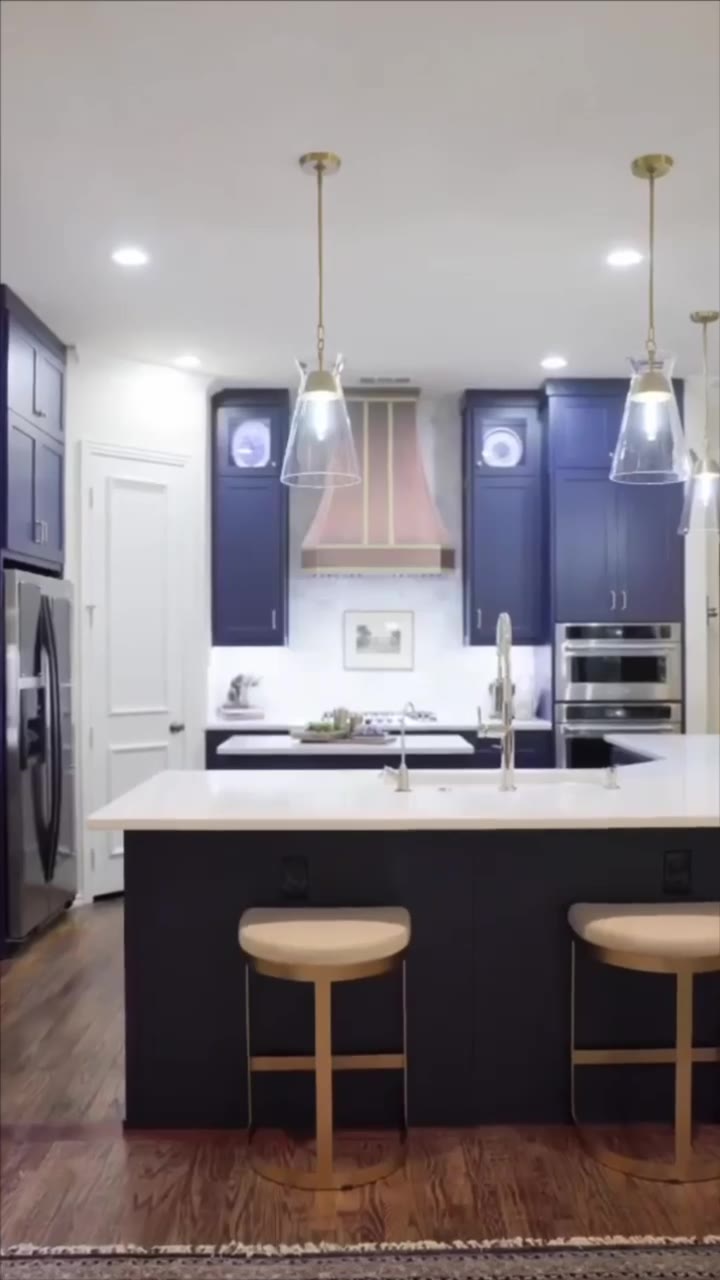 A kitchen in navy cabinetry with a copper hood and a white island.