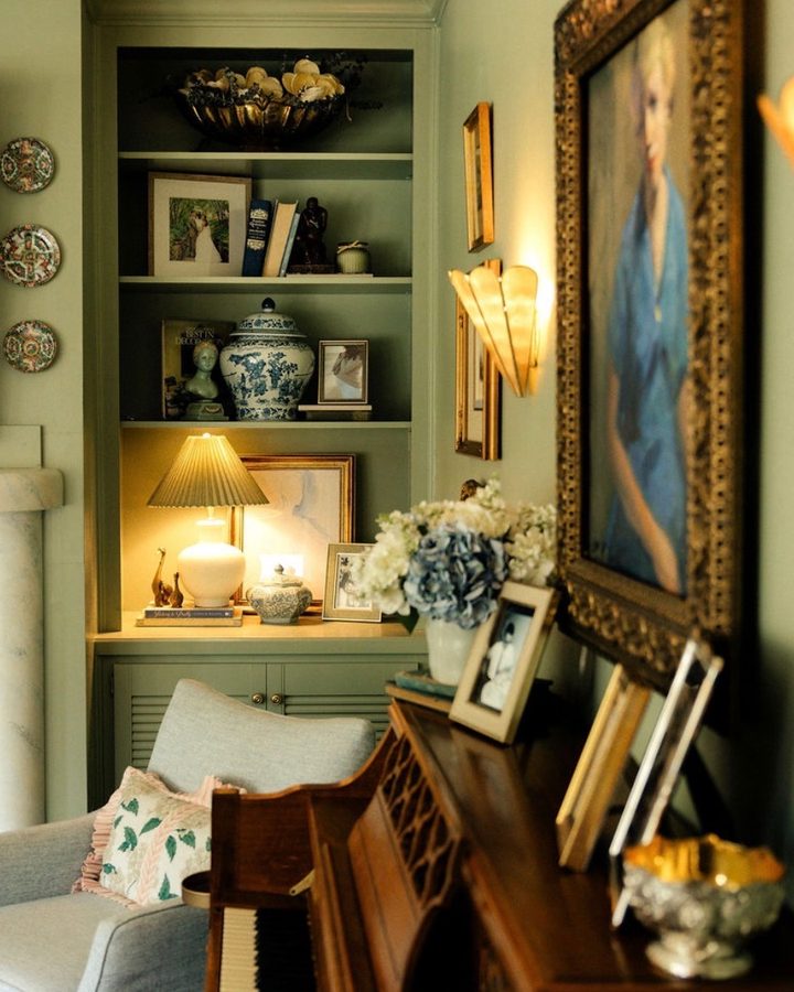 A green study with lit bookshelves, a blue-and-white ginger jar and a gilt-framed portrait above a piano, designed by Anna
